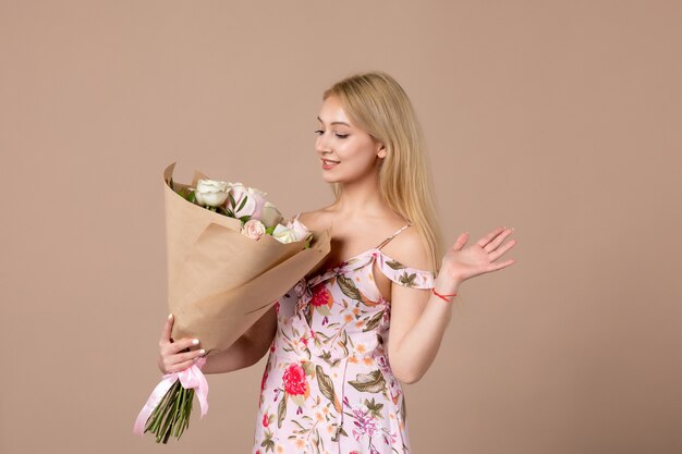Front view of young female holding bouquet of beautiful roses on brown wall