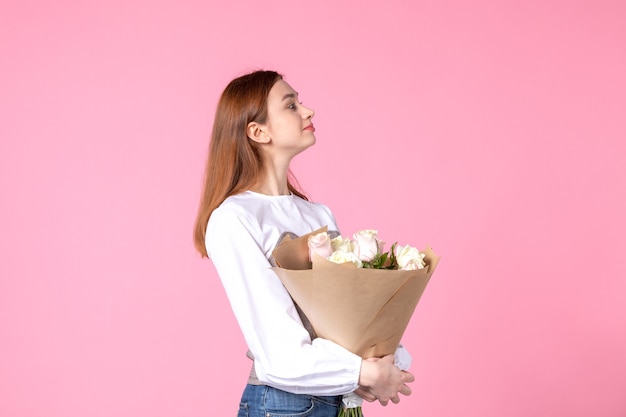 Вид спереди молодая женщина держит букет красивых роз на розовом
