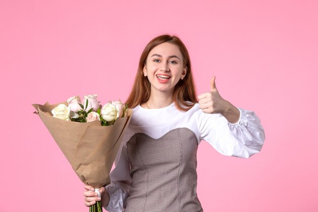 Front view young female holding bouquet of beautiful roses showing awesome gesture on pink