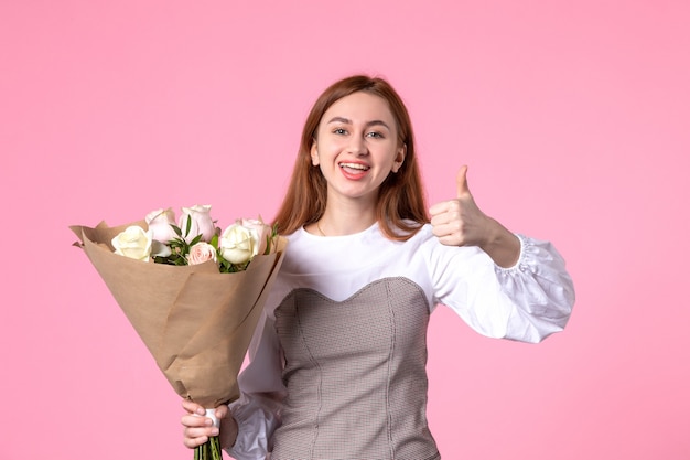 Front view young female holding bouquet of beautiful roses showing awesome gesture on pink