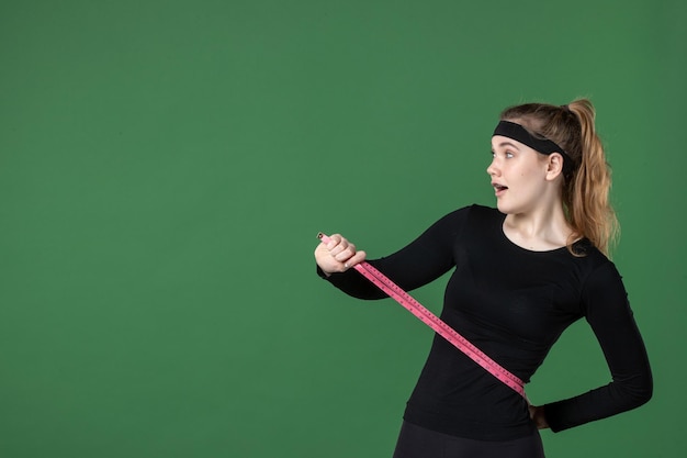 Front view young female holding centimeter for body measuring on green