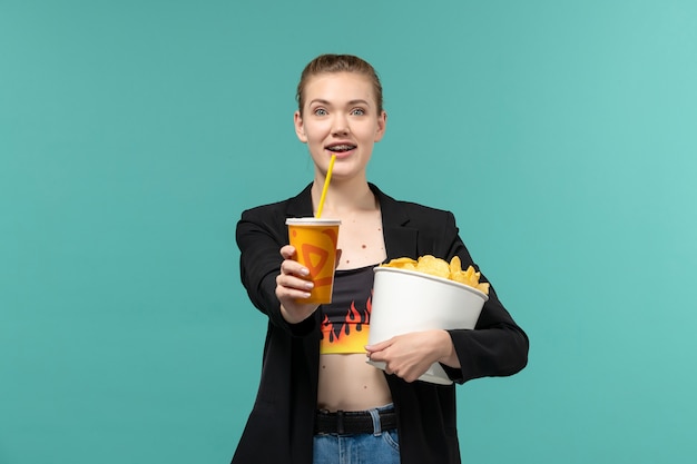 Front view young female holding chips drink and watching movie on the blue surface