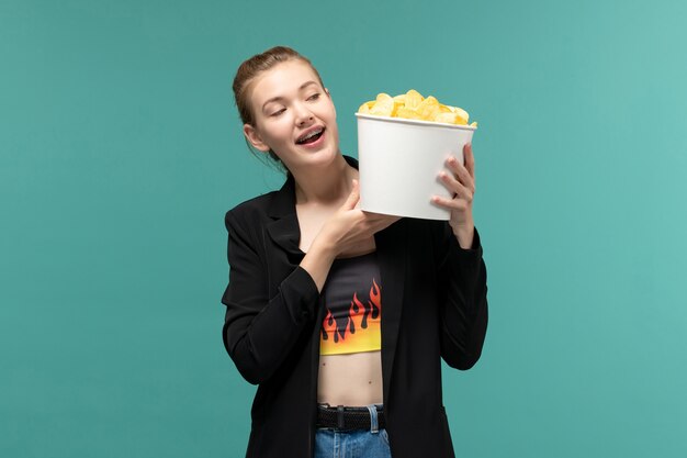 Front view young female holding chips and watching movie on light-blue surface