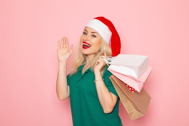 Front view young female holding christmas presents in packages on pink wall xmas model new year holiday