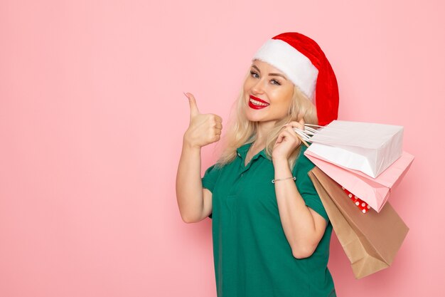 Front view young female holding christmas presents in packages smiling on pink wall xmas photo model new year holiday