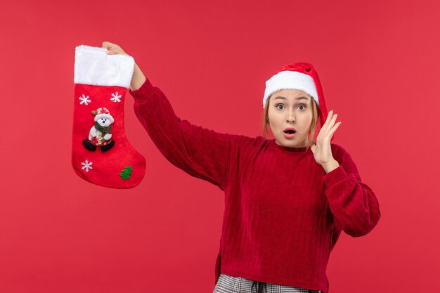 Вид спереди молодая женщина держит рождественский носок на красном полу красный праздник Рождества