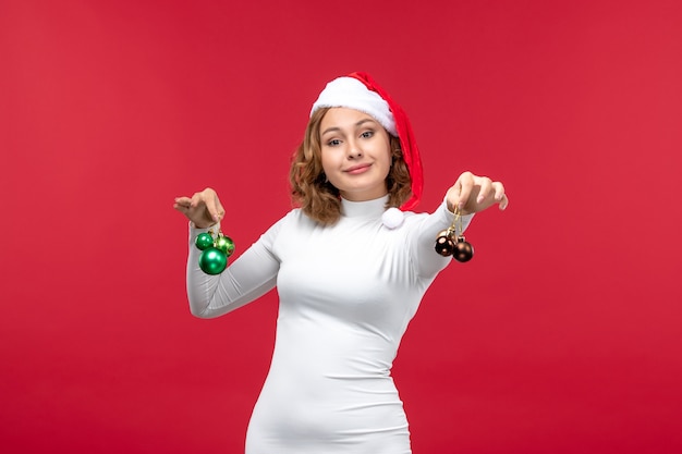 Вид спереди молодой женщины, держащей рождественские игрушки на светло-красном