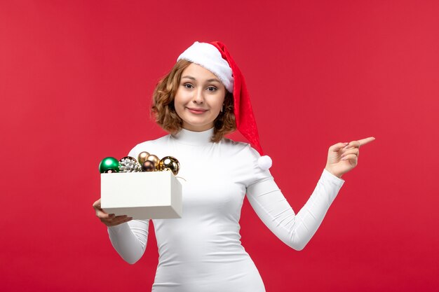 Front view of young female holding christmas toys on red