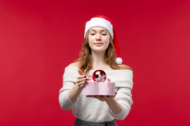 Front view of young female holding christmas toys on red
