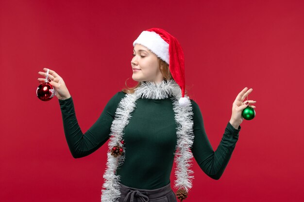 Front view young female holding christmas tree toys on a red background