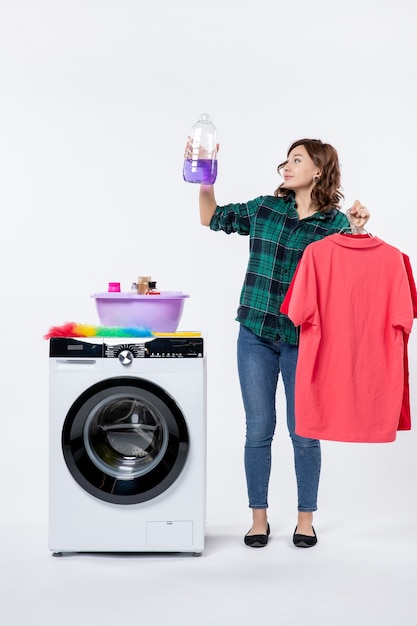 Вид спереди молодой женщины, держащей чистую одежду и жидкий порошок из стиральной машины на белой стене