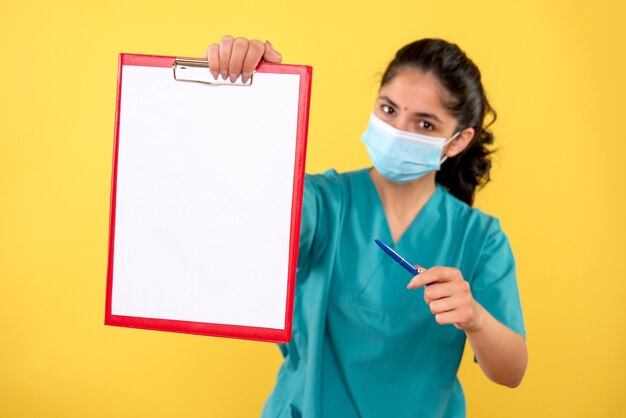 Front view of young female holding clipboard on yellow isolated wall