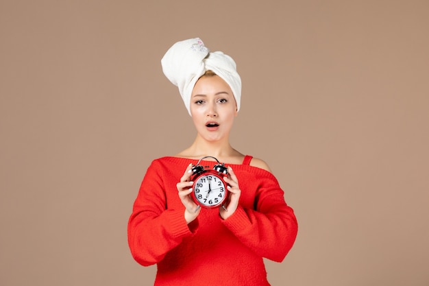 Free photo front view young female holding clocks with towel on her head on brown wall