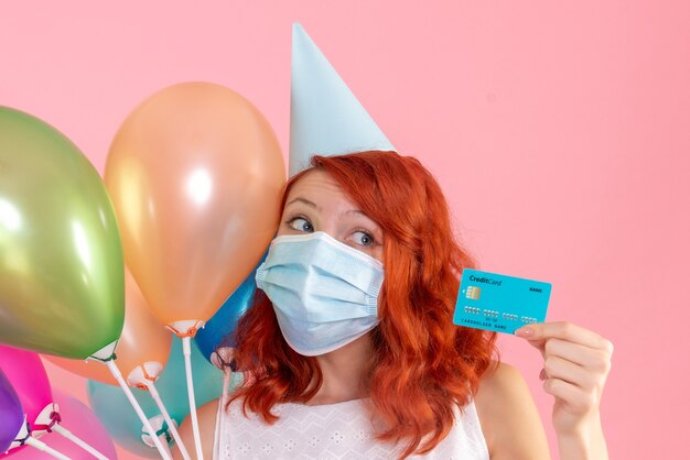 Front view young female holding colorful balloons and bank card on pink 