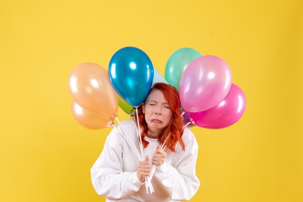 Front view young female holding colorful balloons and fake crying on yellow 