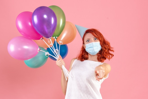 Front view young female holding colorful balloons in mask on a pink 