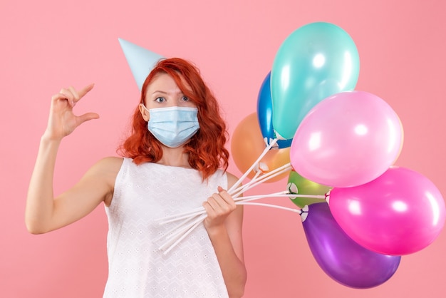 Vista frontale giovane femmina che tiene palloncini colorati in maschera sul rosa