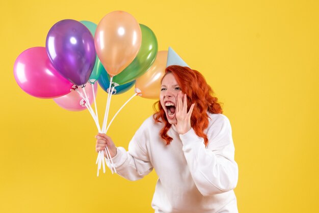 Front view young female holding colorful balloons and screaming on yellow 