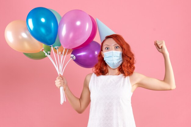 Front view young female holding colorful balloons in sterile mask on a pink 