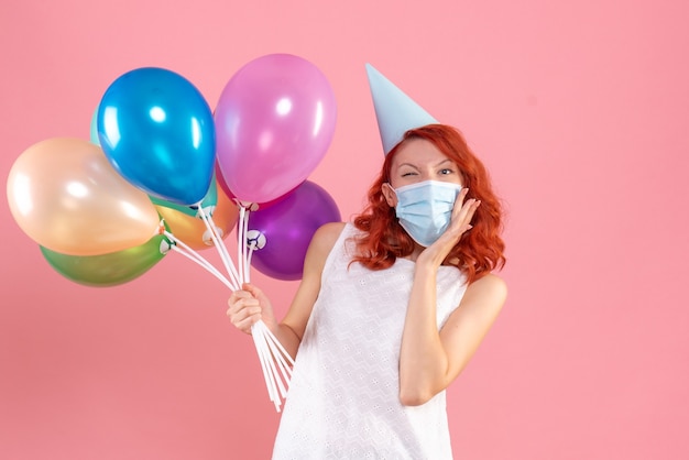 Vista frontale giovane femmina che tiene palloncini colorati in maschera sterile sul rosa