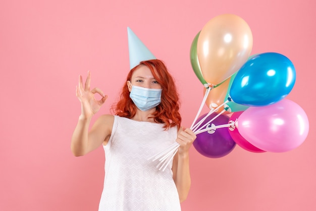 Front view young female holding colorful balloons in sterile mask on a pink 