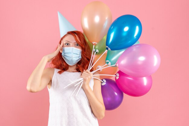 Front view young female holding colorful balloons in sterile mask on a pink 