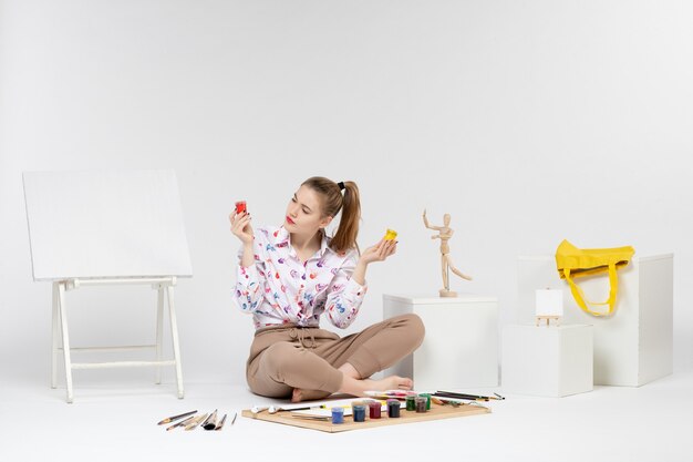 Front view young female holding colorful paints inside cans on white background