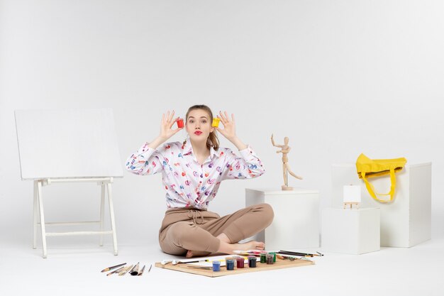 Front view young female holding colorful paints inside little cans on white background