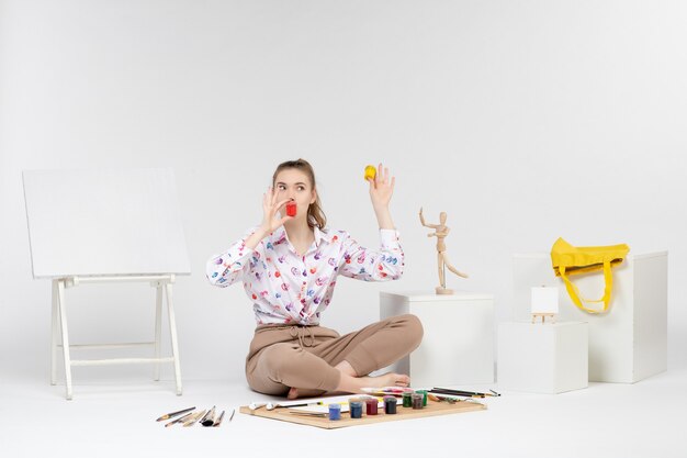 Front view young female holding colorful paints inside little cans on white background