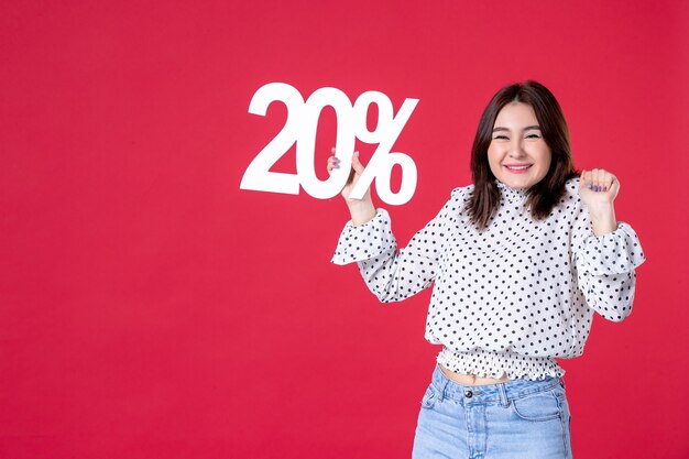 Front view of young female holding discount on red wall