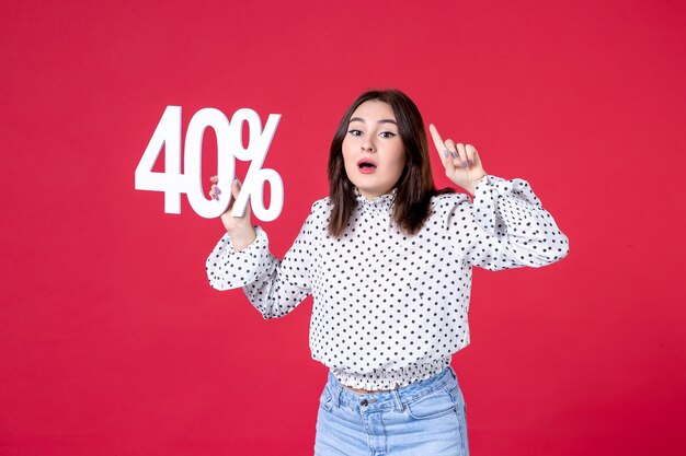 Front view of young female holding discount on red wall