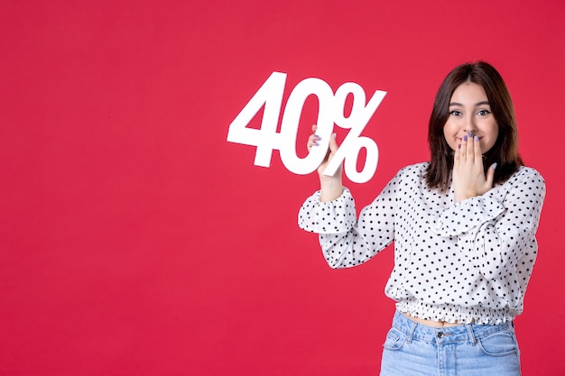 Front view of young female holding discount on red wall