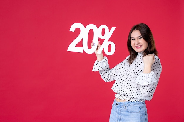 Front view of young female holding discount and rejoicing on red wall