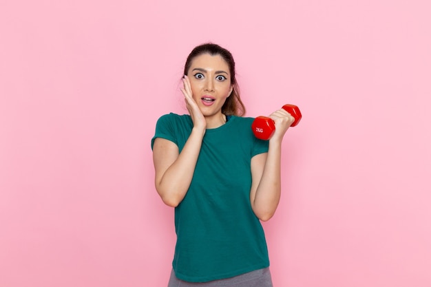 Free photo front view young female holding dumbbells on light pink wall athlete sport exercise health workouts