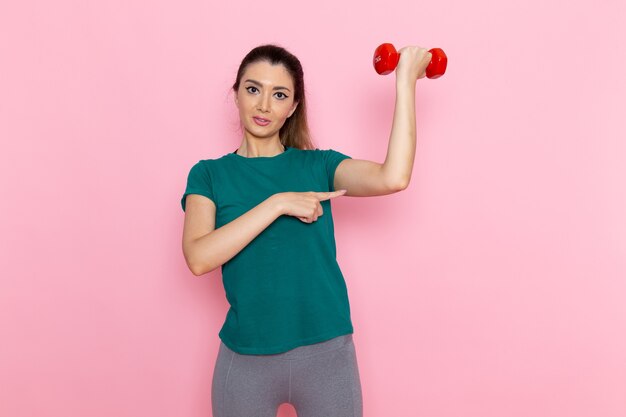 明るいピンクの壁のアスリートスポーツ運動健康トレーニングにダンベルを保持している正面図若い女性