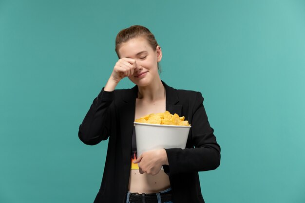 青い表面で泣いている映画を見ているチップを持って食べている若い女性の正面図
