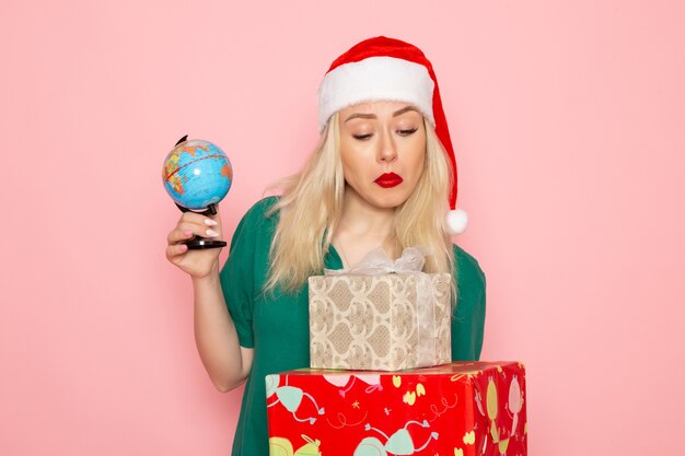 正面図ピンクの壁の写真モデルの女性のクリスマスの新年の色に地球とクリスマスのプレゼントを保持している若い女性