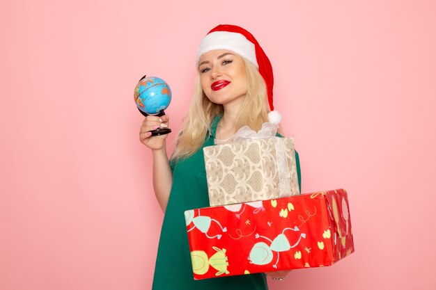 Free photo front view young female holding globe and christmas presents on pink wall photo woman xmas new year color holiday