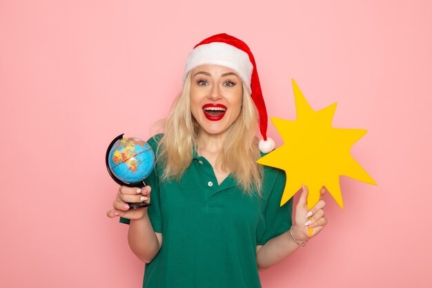 Front view young female holding globe and yellow figure on pink wall model xmas holiday photo new year color