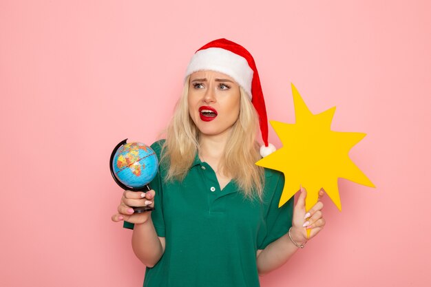 Front view young female holding globe and yellow figure on pink wall photo model woman xmas new year color holiday