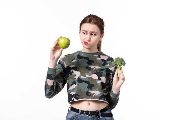 Free photo front view young female holding green apple and little broccoli on white background skin wellness horizontal healthcare juice human fruit