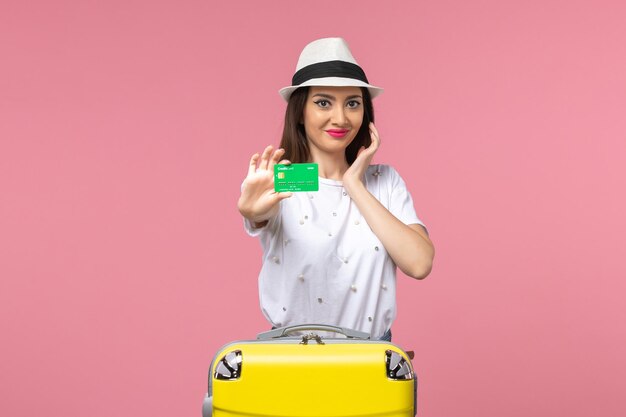 Вид спереди молодая женщина, держащая зеленую банковскую карту на розовой стене, эмоции, летняя женская поездка
