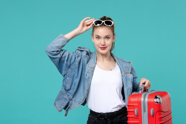 彼女の赤いバッグを保持し、青いdesvoyage休暇旅行旅行の旅行の準備をしている正面図若い女性