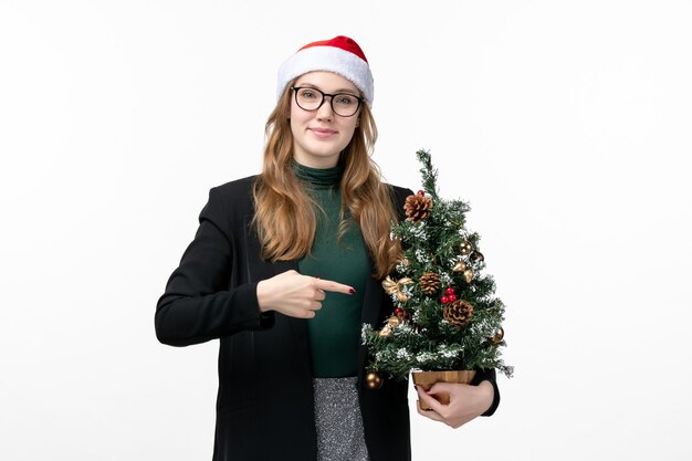 Вид спереди молодая женщина держит праздничную елку на белом полу новогоднюю елочную игрушку