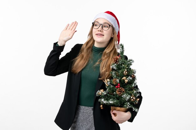 Front view young female holding holiday tree on a white wall new year christmas toy