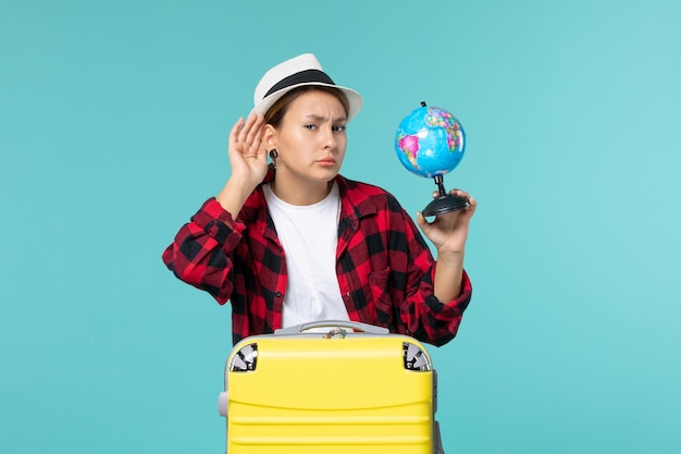 Front view young female holding little globe and preparing for trip on a light-blue space