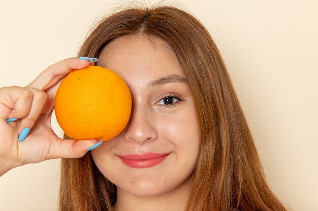 Front view young female holding orange and smiling on grey