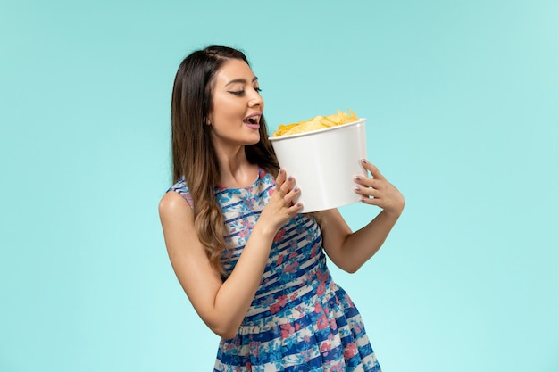 Front view young female holding package with chips on the blue desk