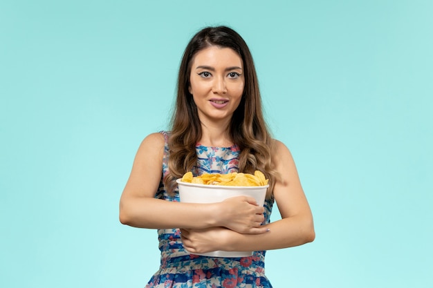 Front view young female holding package with chips on light-blue surface