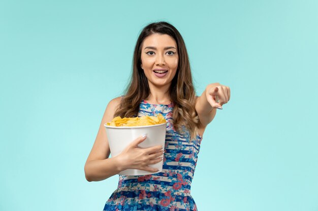 Front view young female holding package with chips and watching movie on blue surface